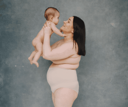 kobieta w połogu w bieliźnie trzyma nad sobą nagie niemowle